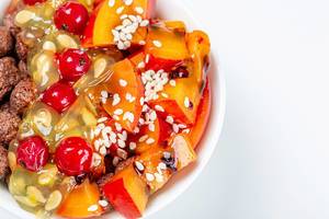 Maisbällchen, Tamarillo Scheiben, Kiwano Horngurke Fruchtfleisch, Sesam, Rote Johannisbeeren und andere Früchte in einer weißen Schale von oben auf weißem Hintergrund fotografiert