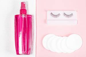 Makeup remover, white towel, cotton pads and false eyelashes on a pink background, top view