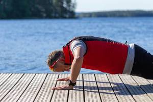 Man doing push-ups during morning work-out, on a wooden walkway with blue water of the deepest lake Finlands "Päijänne " in the background