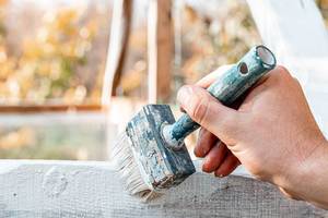 Man hand paints wooden surface with white paint