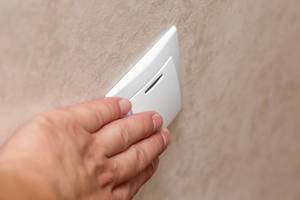 Man hand pressing button for light on wall