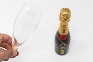 Man holding an empty champagne glass in the hand next to a bottle of Mini Moët on white background