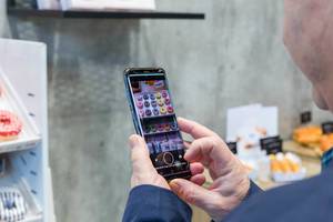 Man uses his smartphone to take a photo of multicoloured donuts on display at the Anuga food fair in Cologne, Germany