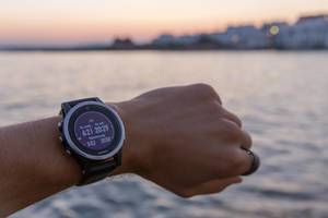 Man wears the Garmin running clock, with sunrise, sunset and twilight time display, in front of the Mediterranean Sea