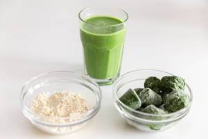 Mandelproteinpulver und gefrorener Spinat in Glasschalen, als Zutaten für einen energiereichen Smoothie