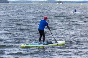 Mann benutzt beim Stand-up-Paddling die Fußschlaufe und paddelt über den Vesijärvi-See in Finnland