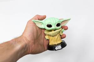 Mann hält die Baby Yoda Pop! Vinylfigur von Star Wars in der Hand vor weißem Hintergrund