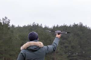 Mann hält Drohne zum Start in die Luft vor Waldstück