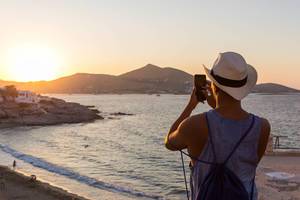 Mann macht Handy-Foto vom Sonnenuntergang an der Küste der griechischen Insel Paros