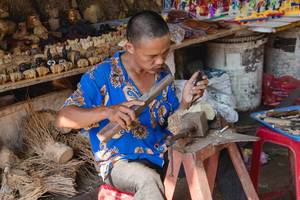 Mann schnitzt eine Holzskulptur und Souvenire auf einer einfachen Werkbank auf einem Markt in Vietnam