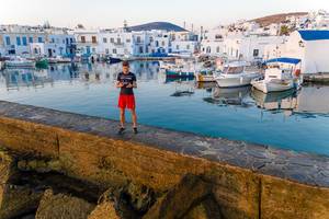 Mann steht auf einer Mauer im Mittelmeer, vor dem Hafen der griechischen Stadt Naoussa und macht Luftaufnahmen mit der Drohne DJI Mavic 2
