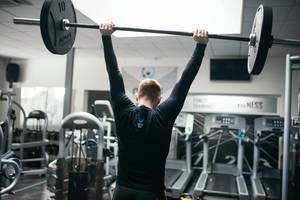 Mann stemmt beim Gewichtheben in Fitnessstudio Langhantel in die Höhe