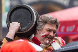Mann trägt beim Kölner Karnevalszug am Rosenmontag ein schwarzes Fass auf dem Rücken