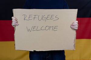 Mann vor deutscher Flagge heißt Flüchtlinge willkommen