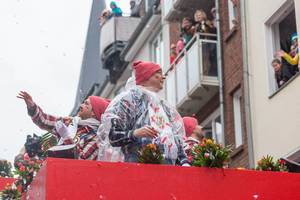 Männer in roter Mütze werfen Strüßjer und begrüßen die Menschen, die am Fenster den Rosenmontagsumzug verfolgen
