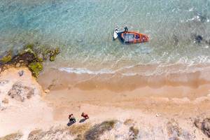 Männer lassen am Santa Maria Strand auf Paros eine Drohne fliegen und machen ein Luftbild von einem Windsurfer, der sein Wassersportgerät abbaut
