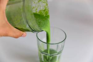 Männerhand schüttet einen gesunden, grünen Smoothie aus Mandelprotein und Spinat in ein Glas