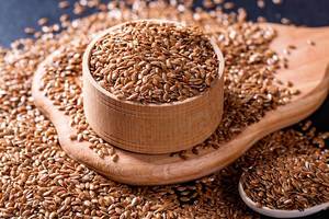 Many flax seeds on a wooden board and black kitchen table