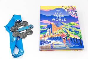 Marathon-Medaillen neben einem Laufstrecken-Buch für Sportler, auf weißer Oberfläche
