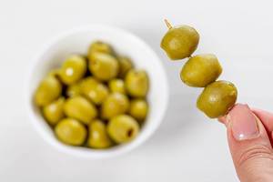 Marinated green olives on a wooden skewer in hand and in a bowl (Flip 2019)