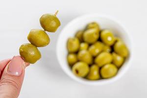 Marinated green olives on a wooden skewer in hand and in a bowl