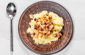 Mashed potatoes with fried onions and bacon in a plate on a white wooden background with a spoon. Top view (Flip 2019)