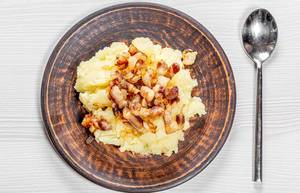 Mashed potatoes with fried onions and bacon in a plate on a white wooden background with a spoon. Top view