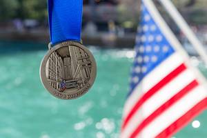 Medal of the 2019 Chicago Marathon with "I am a Marathoner" written on it and a US flag and the river in the background