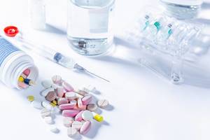 Medizinisches Set mit Spritze, Ampullen, Flasche und verschiedenen Tabletten auf weißem Tisch