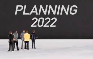 Menschenfiguren stehen vor einer Wand mit  "Planning 2022" als Text