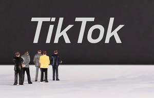 Menschenfiguren stehen vor einer Wand mit  "TikTok" als Text