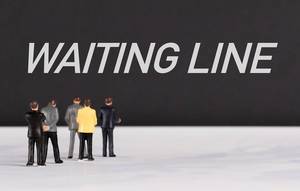 Menschenfiguren stehen vor einer Wand mit  "Waiting Line" als Text