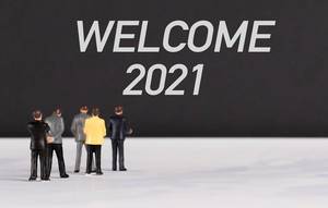 Menschenfiguren stehen vor einer Wand mit  "Welcome 2021" als Text