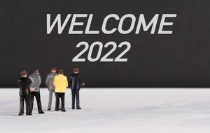 Menschenfiguren stehen vor einer Wand mit  "Welcome 2022" als Text