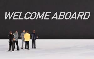 Menschenfiguren stehen vor einer Wand mit  "Welcome Aboard" als Text