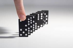 Menschliche Hand dabei eine Reihe von Dominosteinen zum Sturz zu bringen
