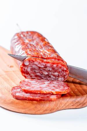 Messer schneidet saftige Salamiwurst auf Holzbrett in feine Scheiben