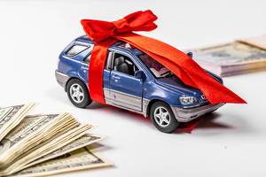 Metal car model with bow and red gift ribbon on white background with dollars (Flip 2019)