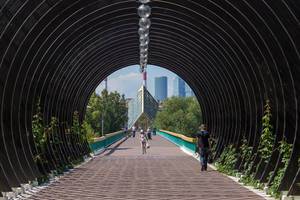 Metal mesh tunnel for climbing plants in Gorky Park. Moscow skyline in the background