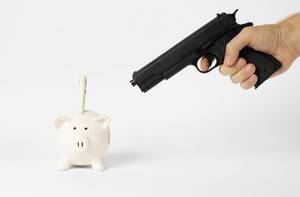 Metaphor of a bank robbery: hand with a gun pointing at a piggy bank with a 50 Euro banknote in it