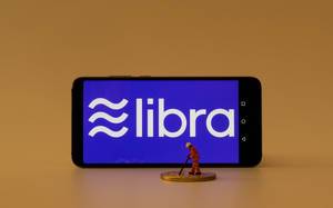 Miniatur Minenarbeiter neben einem Smartphone mit dem Libra Logo auf dem Bildschirm