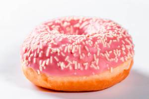 Mit pinker Glasur überzogener frischer Donut mit weißen Streuseln vor weißem Hintergrund