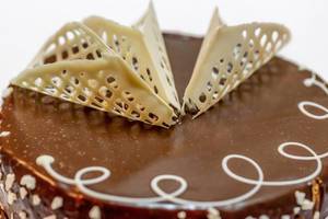 Mit Schokoladenguss überzogener Kuchen, verziert mit gehackten Nüssen und Dekoration aus weißer Schokolade