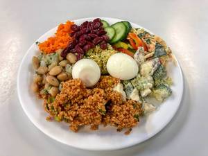 Mixed salad with boiled egg, beans, cucumbers, carrots, broccoli and couscous on white plate