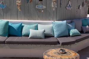 Modern outside furniture with blue and green pillows in front of a white wooden wall