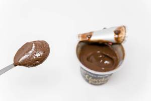 Moussiger High Protein Schokoladenpudding von Ehrmann auf einem Löffen mit Puddingbecher im Hintergrund