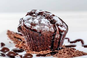 Muffin mit Schokolade, Puderzucker und Schokoladenstücken vor weißem Hintergrund