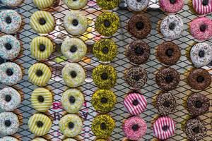 Multicolored view of many donuts displayed in rows with different types of icing