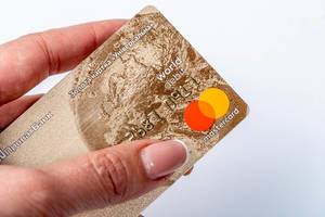 Nahaufnahme einer goldenen Bankkarte / Mastercard, in einer Frauenhand vor weißem Hintergrund