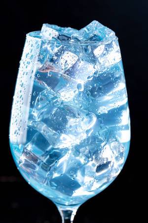 Nahaufnahme eines blauen Cocktails mit Eiswürfeln in einem Glas vor schwarzem Hintergrund